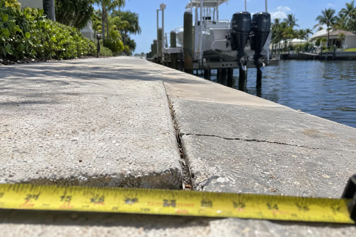 A sunken sidewalk panel with a tape measure across the uneven joint